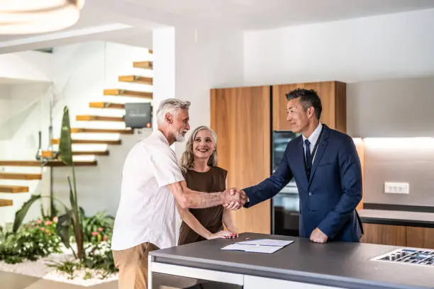 Realtor shaking hands with senior couple in kitchen